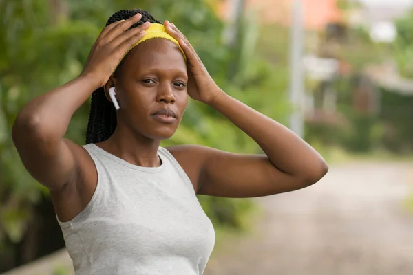 runner girl lifestyle portrait - young attractive and fit black afro American woman adjusting hair band before outdoors running workout at countryside road in sport and fitness concept