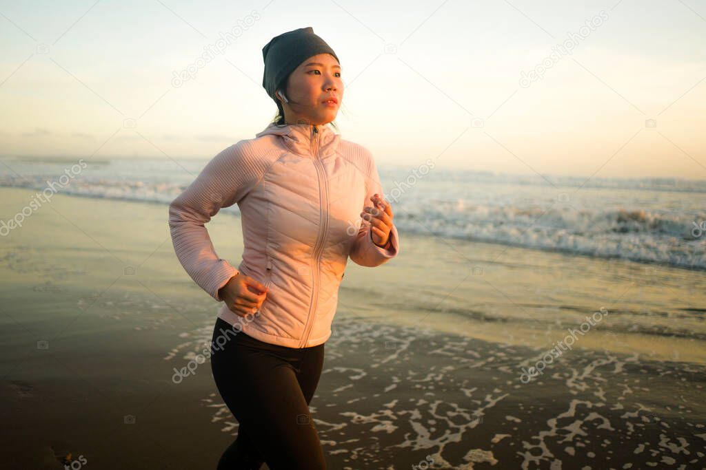 Asian girl running on the beach - young attractive and happy Chinese woman doing jogging workout at beautiful beach enjoying fitness and healthy runner lifestyle