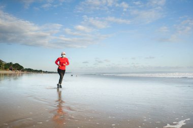 Yüz maskesi takan yeni normal antrenman. 40 'lı ya da 50' li yaşlarda orta yaşlı çekici bir kadın. Sağlıklı yaşam tarzı konseptiyle güzel sahillerde karantina sonrası koşu yapıyor.