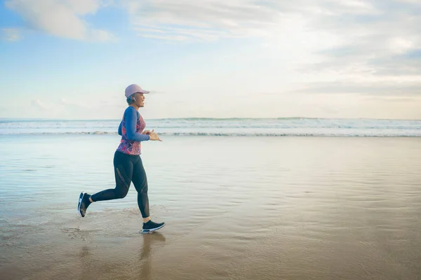 fit and happy middle aged woman running on the beach - 40s or 50s attractive mature lady with grey hair doing jogging workout enjoying fitness and healthy lifestyle at beautiful sea landscape