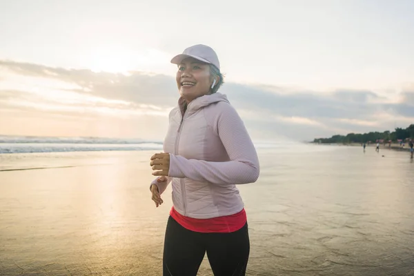 fit and happy middle aged woman running on the beach - 40s or 50s attractive mature lady with grey hair doing jogging workout enjoying fitness and healthy lifestyle at beautiful sea landscape