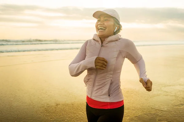 happy and fit middle aged woman running on the beach - 40s or 50s attractive mature lady with grey hair doing jogging workout enjoying fitness and healthy lifestyle at beautiful sea landscape