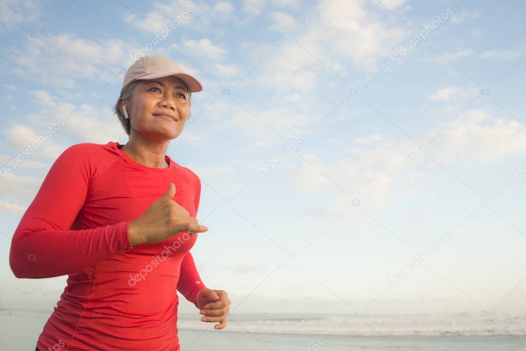 fit and happy middle aged woman running on the beach - 40s or 50s attractive mature lady with grey hair doing jogging workout enjoying fitness and healthy lifestyle at beautiful sea landscape