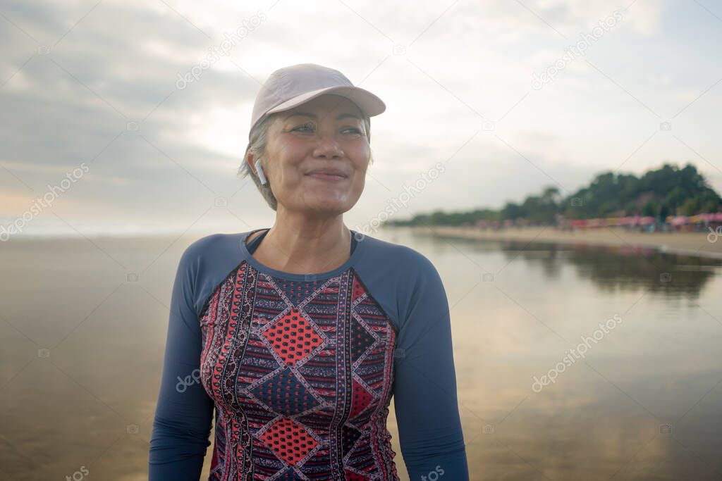 portrait of fit and happy middle aged woman after beach running workout - 40s or 50s attractive mature lady with grey hair smiling cheerful after jogging enjoying fitness and healthy lifestyle