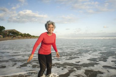 Formda ve orta yaşlı bir kadının plaj koşusundan sonraki hayat tarzı portresi. 40 'lı ya da 50' li yaşlarda, spor yaparken keyifli bir şekilde koştuktan sonra gülümseyen gri saçlı, olgun bir kadın.