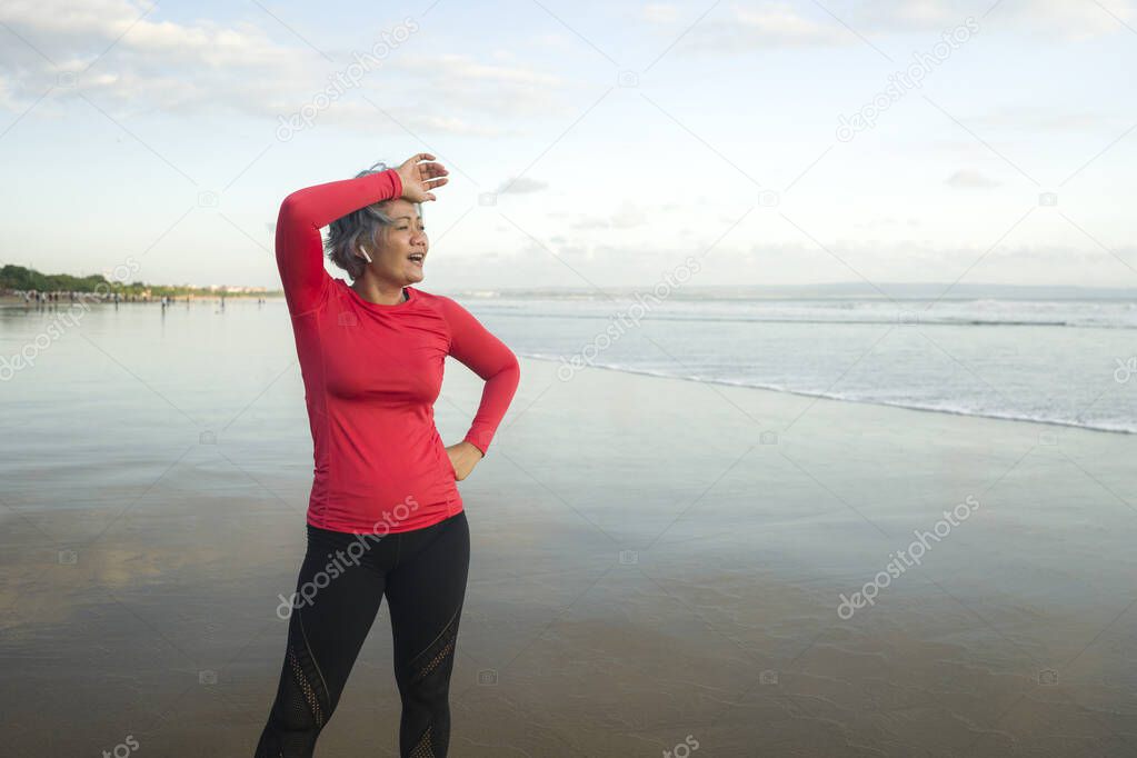 lifestyle portrait of fit and tired middle aged woman after beach running workout - 40s or 50s attractive mature lady with grey hair breathing exhausted after jogging 