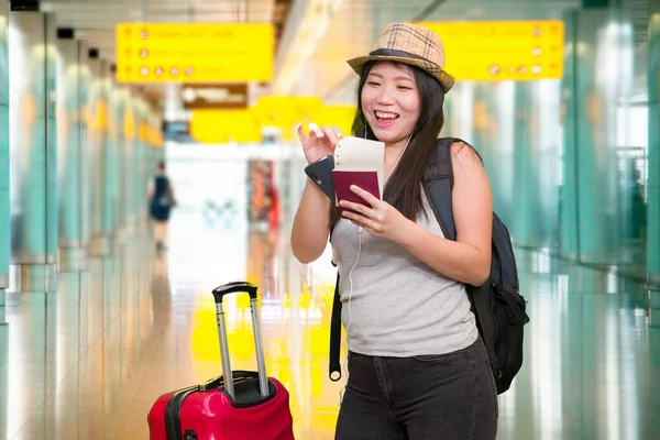 young Asian girl traveling happy and excited - young attractive and beautiful Korean woman with trolley suitcase at airport departures enjoying holiday travel smiling cheerful