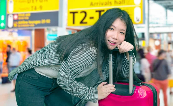 young Asian girl traveling happy and excited - young attractive and beautiful Korean woman with trolley suitcase at airport departures enjoying holiday travel smiling cheerful