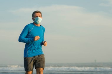Yeni normal plaj koşusu antrenmanı. Genç fit ve çekici bir adam. Yüzü maske takarak denizde çıplak koşuyor. 