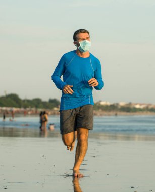 Yeni normal plaj koşusu antrenmanı. Genç fit ve çekici bir adam. Denizde çıplak ayakla koşuyor.