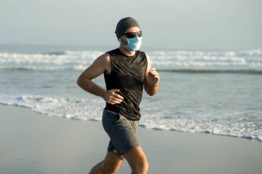 Yeni normal plaj koşusu egzersizi - sağlıklı yaşam tarzı konseptinde özgür hissederek deniz eğitiminden sonra çıplak ayak koşan yüzü maskeli genç ve çekici bir adam.
