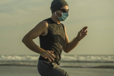 Yeni normal plaj koşusu egzersizi - sağlıklı yaşam tarzı konseptinde özgür hissederek deniz eğitiminden sonra çıplak ayak koşan yüzü maskeli genç ve çekici bir adam.
