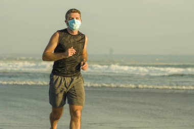 Yeni normal plaj koşusu egzersizi - sağlıklı yaşam tarzı konseptinde özgür hissederek deniz eğitiminden sonra çıplak ayak koşan yüzü maskeli genç ve çekici bir adam.