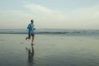 Açık hava koşusu antrenmanı. Genç çekici ve atletik koşucu. Yaz aylarında güzel plajlarda koşuyor. 
