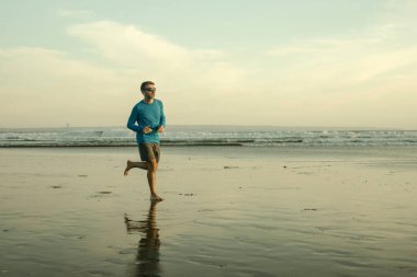 Açık hava koşusu antrenmanı. Genç çekici ve atletik koşucu. Yaz aylarında güzel plajlarda koşuyor. 