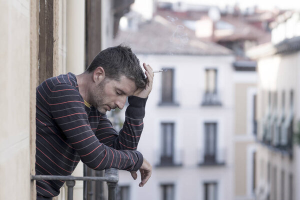 urban lifestyle emotional portrait of young handsome man sad and depressed smoking cigarette thoughtful at home balcony leaning unhappy feeling bittered   suffering some problem