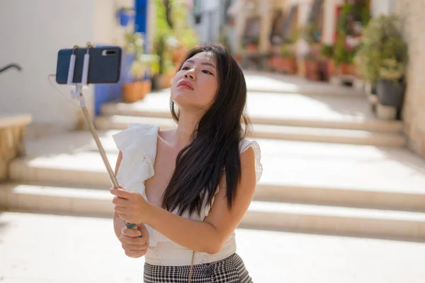 Asian girl taking self portrait on the street - young happy and attractive Asian Japanese woman visiting Seville in Spain taking selfie enjoying beautiful old city tour cheerful and relaxe