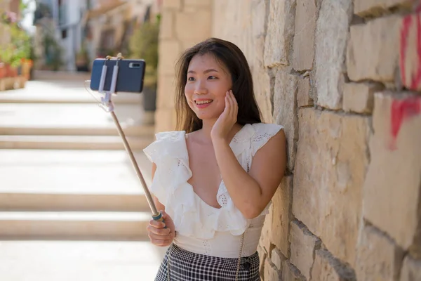 Asian girl taking self portrait on the street - young happy and attractive Asian Korean woman visiting Seville in Spain taking selfie enjoying beautiful old city tour cheerful and relaxe