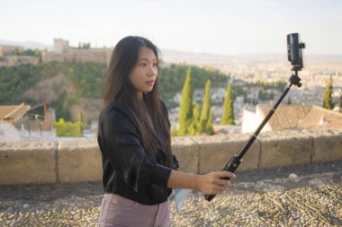Avrupa 'da yaz tatili geçiren güzel ve mutlu Asyalı Koreli bir turistin portresi. İspanya' nın güzel Alhambra 'sında cep telefonuyla selfie çekiyor.