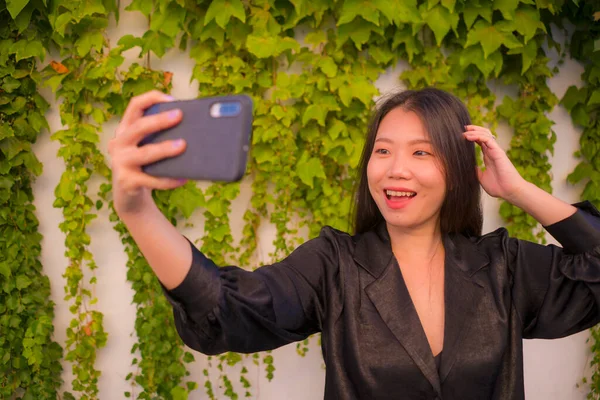 young happy and beautiful Asian Japanese woman enjoying outdoors taking selfie with mobile phone at village garden playful and carefree in beauty fashion and freedom concept