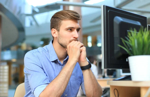 Ung man sitter och tittar på datorskärm medan arbetande i kontor. — Stockfoto