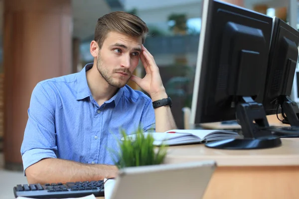 Młody mężczyzna siedząc i patrząc na monitor komputera podczas pracy w biurze. — Zdjęcie stockowe