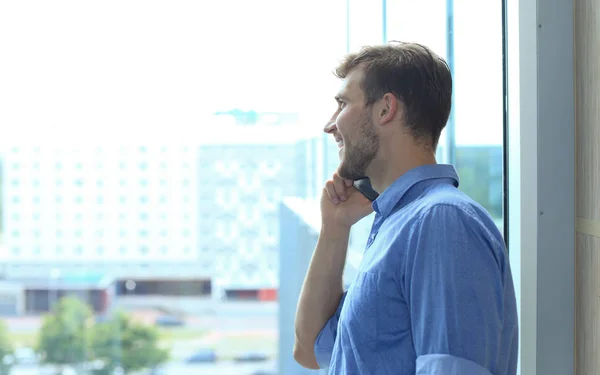 Hombre de negocios sonriente de pie y usando el teléfono móvil en la oficina . — Foto de Stock