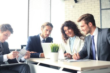 Girişim ekibi, modern parlak ofis içinde toplantı ve dizüstü bilgisayar üzerine çalışıyor