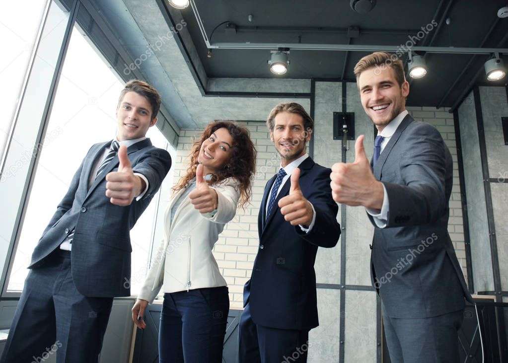 Portrait of happy businesspeople standing in office showing thumbs up