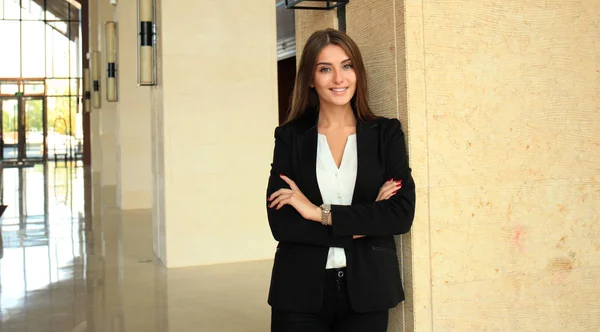 腕を近代的なオフィスに組んで立っている若い美しい女性実業家 — ストック写真
