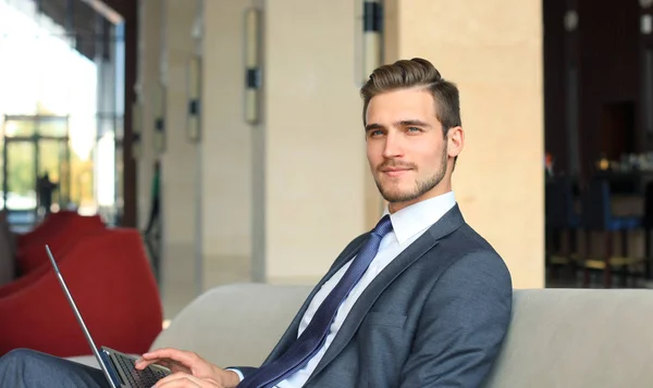 Young businessman working on laptop, sitting in hotel lobby waiting for someone