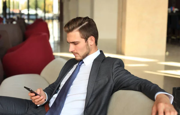 Young businessman sitting relaxed on sofa at hotel lobby making a phone call, waiting for someone