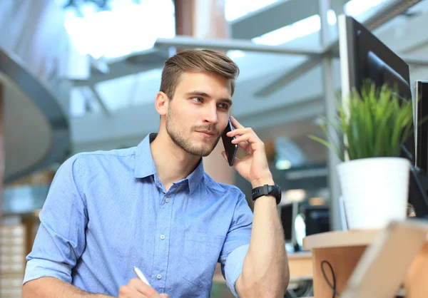 Uśmiechający się biznesmen siedzi i przy użyciu telefonu komórkowego w biurze. — Zdjęcie stockowe