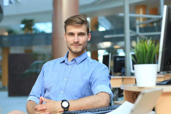 Porträtt av lycklig man sitter vid skrivbord, tittar på kameran, leende. — Stockfoto