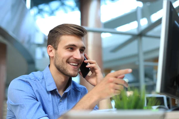 Uomo d'affari sorridente seduto e utilizzando il telefono cellulare in ufficio . — Foto Stock