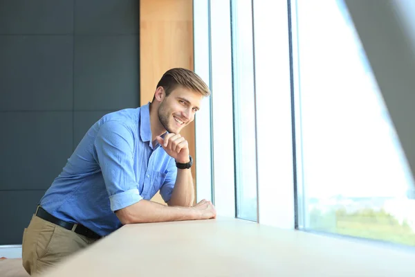 Молодий чоловік стоїть біля вікна у своєму офісі, думаючи про свої цілі . — стокове фото