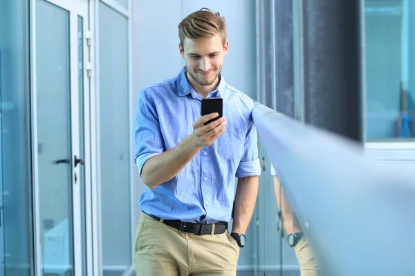 Usmívající se podnikatel stojící a používání mobilních telefonů v kanceláři. — Stock fotografie