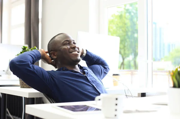 Relajado hombre de negocios afroamericano sentado en su escritorio mirando al aire. —  Fotos de Stock