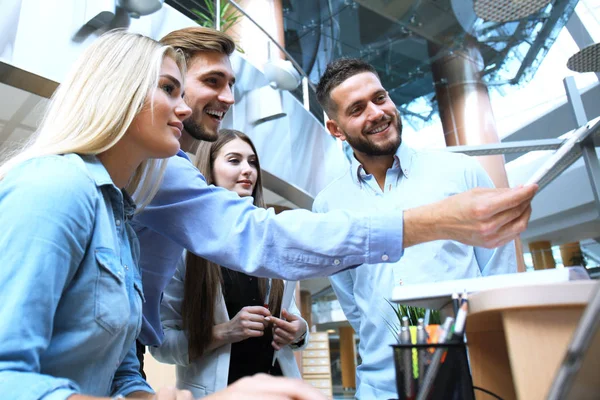 Grupo de jóvenes en ropa casual sentados en el escritorio de la oficina y discutiendo algo mientras miran PC juntos . — Foto de Stock