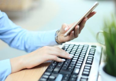 Ofiste masasında akıllı telefon kullanarak klavye yazarak kadın eller.