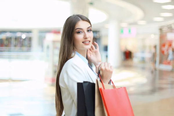 Lycklig kvinna som håller i shoppingväskor och ler mot gallerian. — Stockfoto