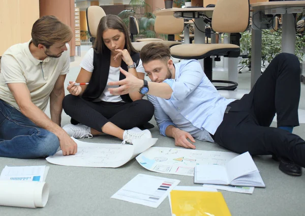 Groep van jonge ondernemers en ontwerpers kijken naar projectplan aangelegd op verdieping. Ze werken aan nieuw project. — Stockfoto