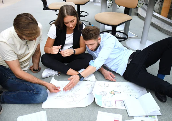 Група молодих бізнесменів і дизайнерів, які дивляться на план проекту, викладений на підлозі. Вони працюють над новим проектом . — стокове фото