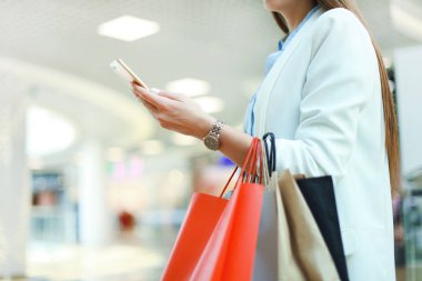 Smartphone kullanarak ve alışveriş çantası dururken alışveriş arka plan üzerinde tutan kadın.