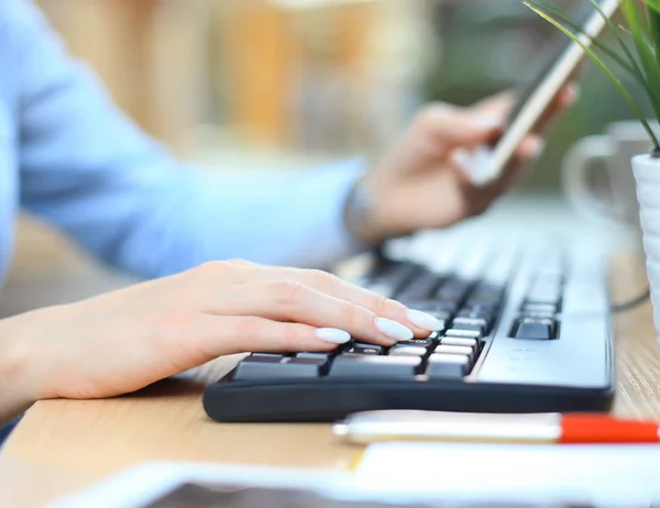 Closeup vrouwelijke handen typen op toetsenbord met behulp van slimme telefoon op het Bureau in het kantoor. — Stockfoto