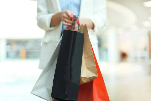 Woman using smartphone and holding shopping bag while standing on the mall background. — Stock Photo, Image