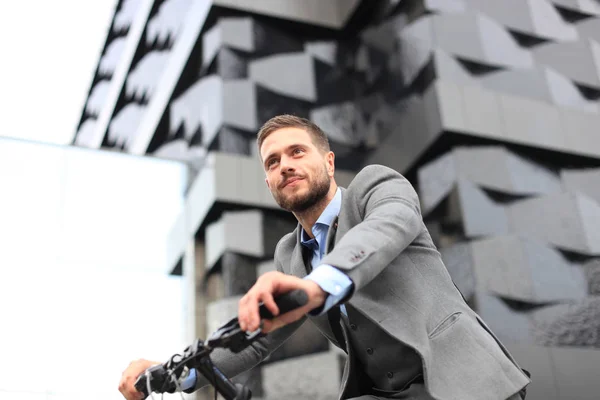 Guapo joven hombre de negocios montar en bicicleta al aire libre en la ciudad . — Foto de Stock