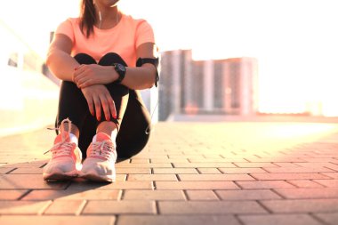 Cep telefonu ve müzik, açık günbatımı veya gündoğumu şehirde sokakta oturan genç çekici sportif kız.