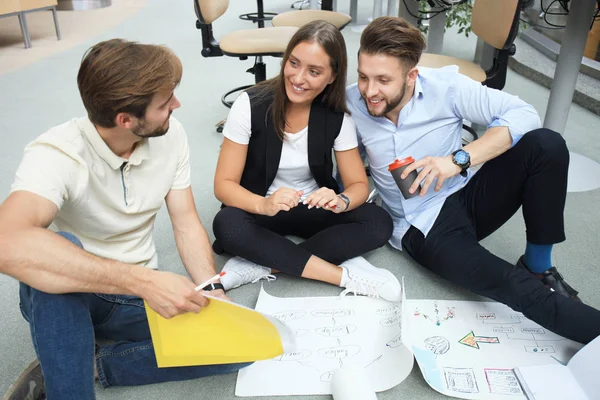 Groep van jonge ondernemers en ontwerpers kijken naar projectplan aangelegd op verdieping. Ze werken aan nieuw project. — Stockfoto