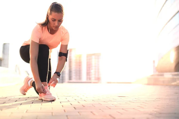 Jonge fitness aantrekkelijke sportieve meisje runner verbindt de schoenveters op haar sportschoenen klaar om te lopen. — Stockfoto